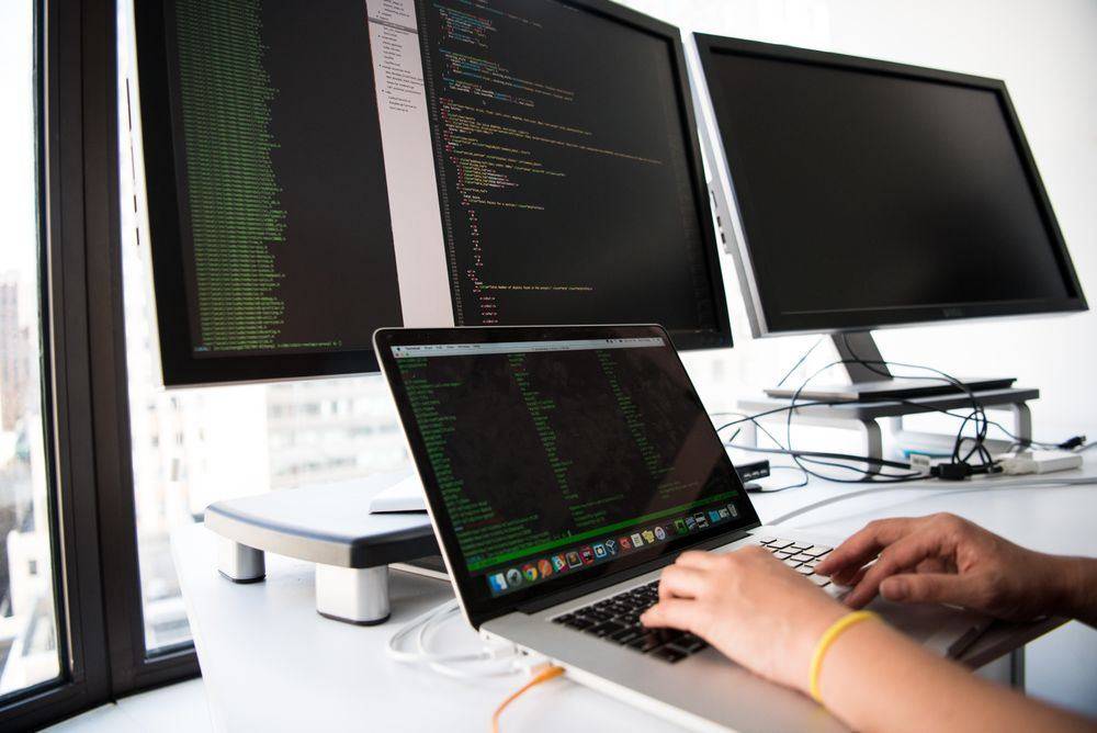Developer writing code on a laptop in front of multiple monitors